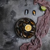 Draufsicht auf köstliche Muscheln mit Muscheln auf Vintage-Teller und Limette mit Zitrone und Tuch auf grau