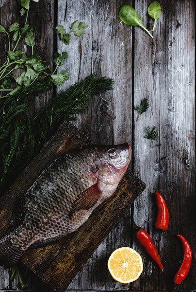 top view of fresh raw sea fish with herbs and chili peppers on rustic wooden table