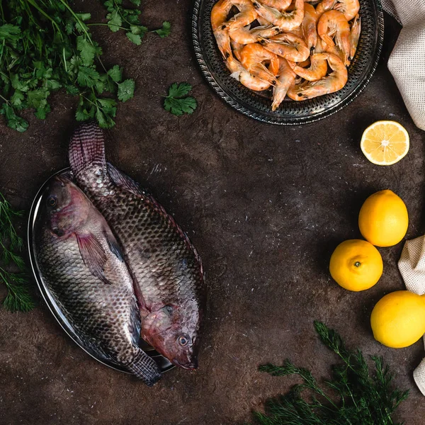 top view of raw fish, shrimp, herbs and lemons on dark table top