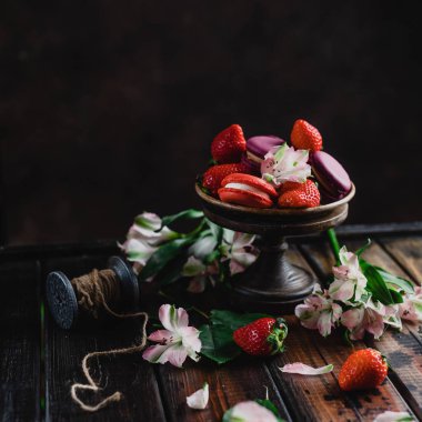 tatlılar macarons ve çiçekler ile ahşap masa üzerinde çilek ile kase