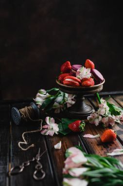 macarons ve çiçekler ile ahşap masa üzerinde çilek ile kase