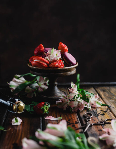 bowl with macarons and strawberries on wooden table with flowers and champagne bottle and scissors, 