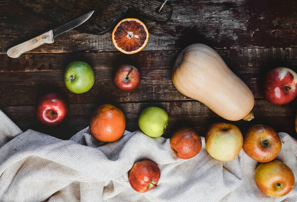 top view of pumpkin, apples, blood oranges, kitchen towel and knife on wooden table 