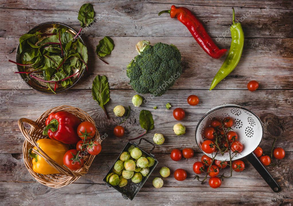Top view of wicker basket, plate, colander, cherry tomatoes, peppers, mangold leaves, broccoli and brussel sprouts