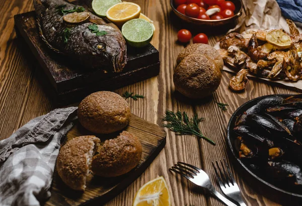 Surtido de mariscos y pescados al horno con pan y tomates en mesa de madera - foto de stock