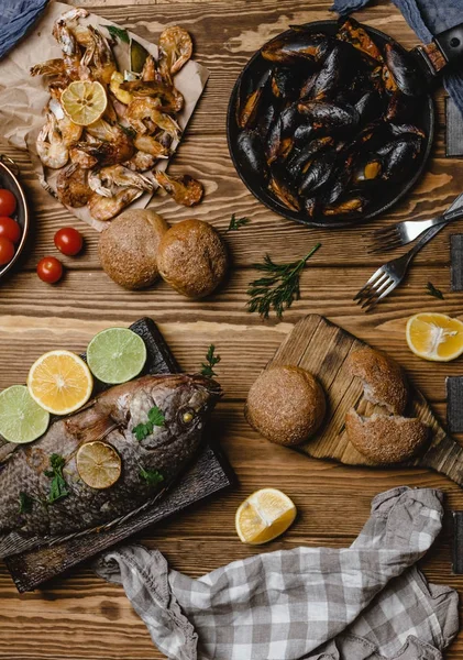 Top view of assorted seafood and baked fish with bread and tomatoes on wooden table — Stock Photo