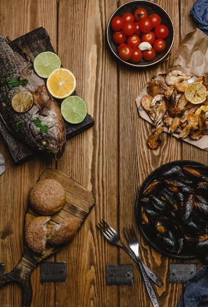Вид зверху асорті з морепродуктів і запеченої риби з хлібом і помідорами на дерев'яному столі — стокове фото
