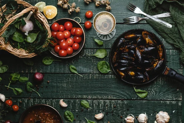 Vue de dessus des moules cuites avec coquilles servies dans une casserole avec tomates, herbes et vin sur une table rustique — Photo de stock