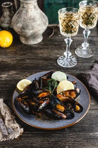 Cozze cotte con conchiglie servite sul piatto con due bicchieri di vino bianco sul tavolo di legno — Foto stock