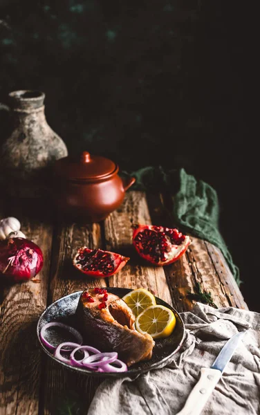 Baked salmon steak with lemon and onion on plate with pomegranate on wooden table — Stock Photo