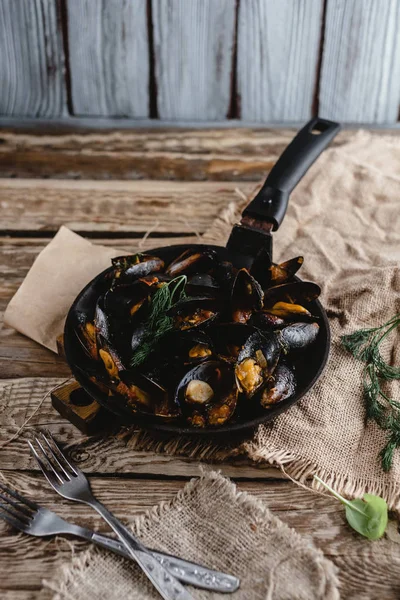 Vista de cerca de deliciosos mejillones fritos con conchas en la sartén y tenedores en la mesa - foto de stock