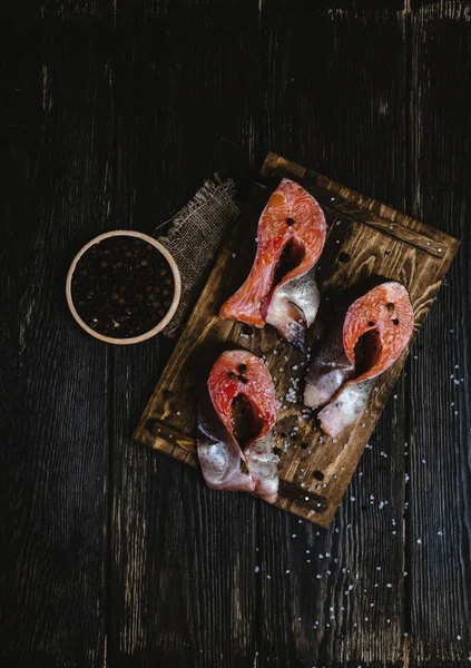Top view of sliced salmon fish on wooden cutting board with sackcloth, salt and peppercorns on rustic table — Stock Photo