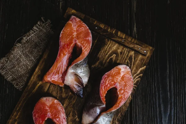 Vista superior de pescado de salmón fresco en rodajas sobre tabla de cortar de madera con saco sobre mesa rústica - foto de stock