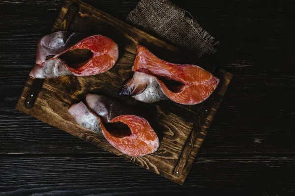 Vista superior de pescado de salmón en rodajas sobre tabla de cortar de madera con saco sobre mesa rústica - foto de stock