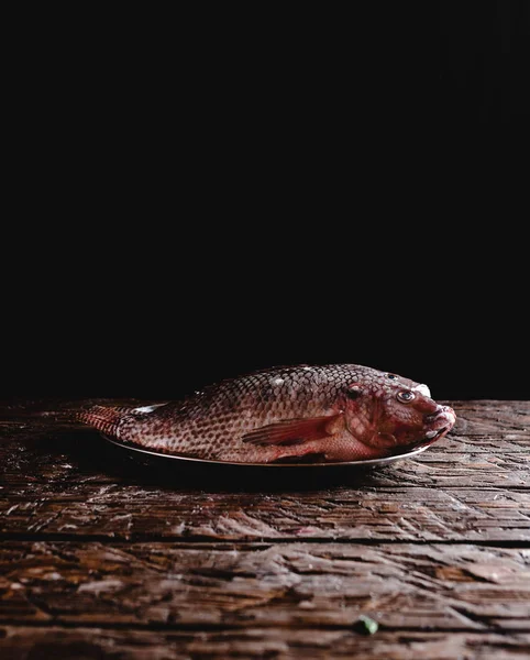 Крупним планом вид свіжої сирої морської риби на старовинній тарілці на сільському дерев'яному столі — стокове фото