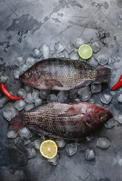 Vue de dessus des poissons de mer crus frais sur des glaçons avec des tranches de citron vert et de citron et des piments sur gris — Photo de stock