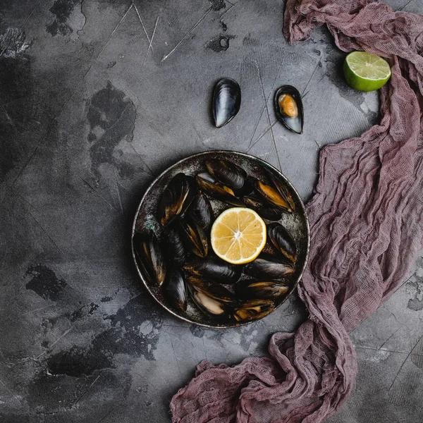 Vista superior de deliciosos mejillones con conchas en plato vintage y lima con limón y tela en gris — Stock Photo