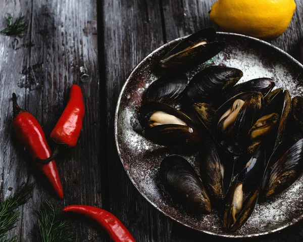 Vista ravvicinata di deliziose cozze su piatto vintage e peperoncini al limone su tavolo rustico in legno — Foto stock