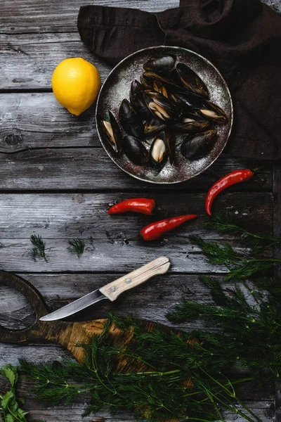 Vue de dessus de délicieuses moules aux coquilles sur assiette vintage aux herbes, piments et citron sur table rustique en bois — Photo de stock