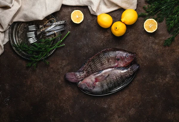 Vista superior de pescado crudo sano en plato y limones con hierbas en la parte superior de la mesa oscura - foto de stock