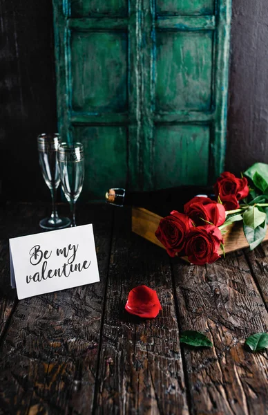 Soyez ma carte de voeux de Saint-Valentin, roses rouges et bouteille de champagne avec des verres sur la table minable — Photo de stock