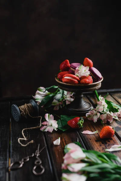 Bowl with macarons and strawberries on wooden table with flowers — Stock Photo