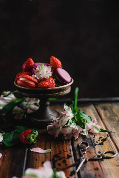 Bowl with macarons and strawberries on wooden table with flowers and scissors — Stock Photo