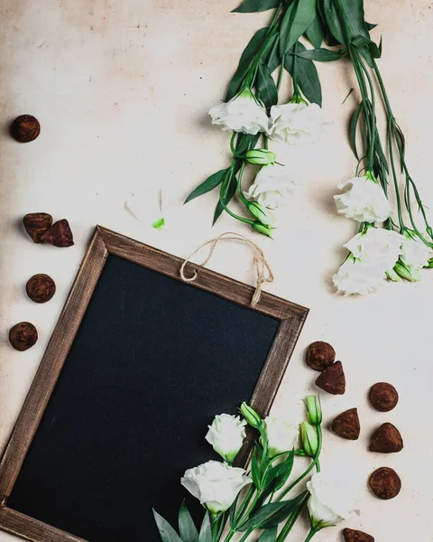 Vista superior de quadro negro em moldura de madeira com flores eustoma e doces de chocolate — Fotografia de Stock