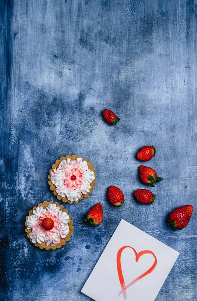 Vista superior de fresas, tartas y tarjeta de felicitación con el corazón en el fondo malhumorado para el día de San Valentín - foto de stock