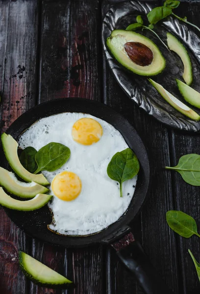 Top view of fried eggs with spinach and avocado pieces on wooden tabletop — Stock Photo