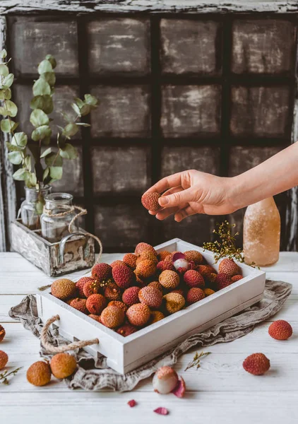 Cropped image of female hand and pile of lychees in wooden box on table — Stock Photo