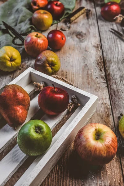 Closeup view of pears, apples, wooden box, scissors, hand scales and kitchen towel on rustic tabletop — Stock Photo