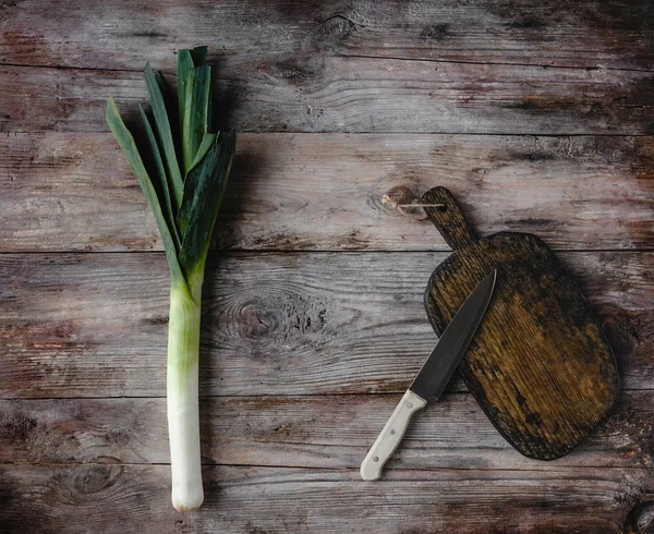 Top view of cutting board, knife and leek on rustic wooden table — Stock Photo