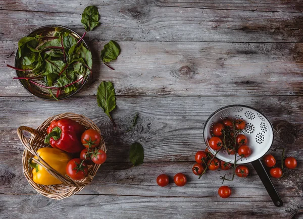 Top view of wicker basket, plate, colander, cherry tomatoes, peppers and mangold leaves on wooden table — Stock Photo