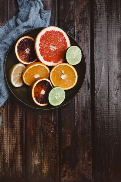 Vista superior de mitades de naranja, pomelo, lima, naranja sangre y limón en plato y toalla de cocina sobre mesa de madera — Stock Photo