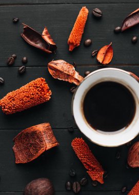 Kuru otlar ve koyu ahşap masa üzerinde kahve çekirdekleri ile sıcak kahve