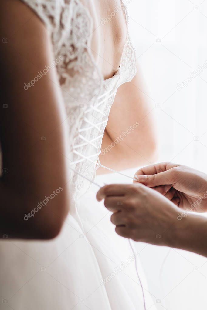 bridesmaid's hands helping with bride's white dress. Wedding day