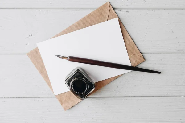 set of vintage dip pen, inkpot and blank paper sheet with envelope on white wooden table