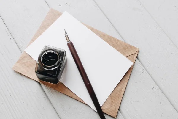 set of vintage dip pen, inkpot and blank paper sheet with envelope on white wooden table