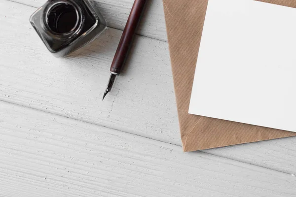 set of vintage dip pen, inkpot and blank paper sheet with envelope on white wooden table