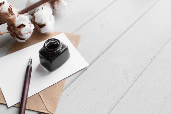 set of vintage dip pen, inkpot, blank paper sheet, envelope and cotton branch on white wooden table