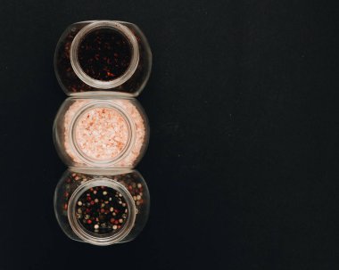 cam kutu aromalı tuz, çeşitli peppercorns ve siyah arka plan üzerinde kırmızı baharat