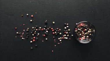 glass with assorted peppercorns on black background clipart