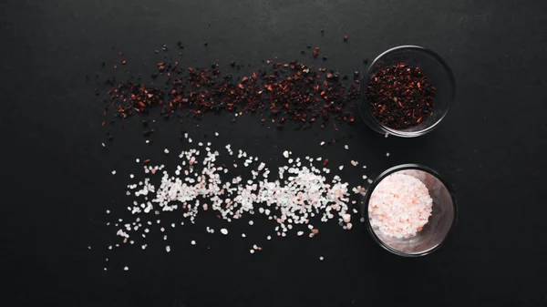 glasses with flavored salt and red spice on black background