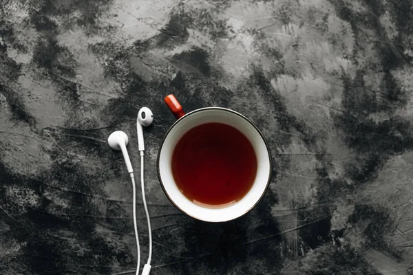 white modern earphones and cup of tea on black stone background