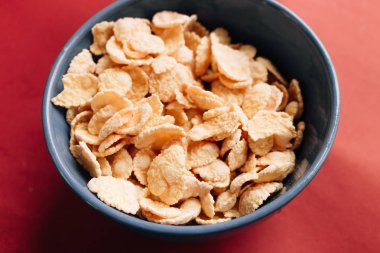 Kırmızı arka planda kasede mısır gevreği ve sağlıklı bir kahvaltı.