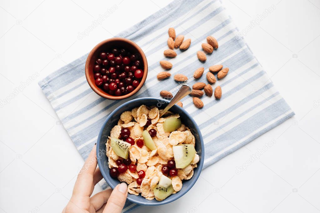 delicious crispy cornflakes with kiwi pieces and cranberries in bowl, almonds on dish cloth, closeup, healthy breakfast 