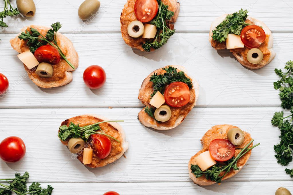 delicious fresh bruschettas with tomatoes and parsley, traditional Italian cuisine, ingredients on white wooden table