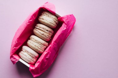 Lila arka plan, tatlı tatlı pembe kağıt kutusunda lezzetli renkli macaroons 