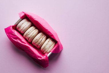 Lila arka plan, tatlı tatlı pembe kağıt kutusunda lezzetli renkli macaroons 